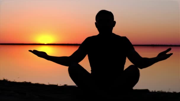 Una silueta de un hombre, meditando en una costa contra el atardecer — Vídeo de stock