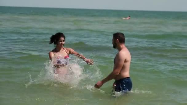 Una pareja juega en un agua de mar. Se cortan mutuamente. Entonces el joven se da por vencido y cae al agua — Vídeo de stock