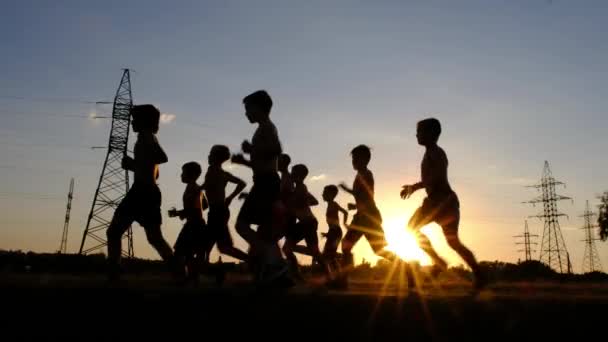 Siluetter av unga pojkar, jogging på en utbildning mot solnedgången — Stockvideo