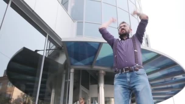 Чоловік дуже схвильований. Він ходить, кричить і піднімає руки проти високих будівель — стокове відео