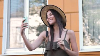 Bir şapka ve uzun bir elbise genç bir kadın selfie, yapım o zaman denetler ve bir tane daha yapar