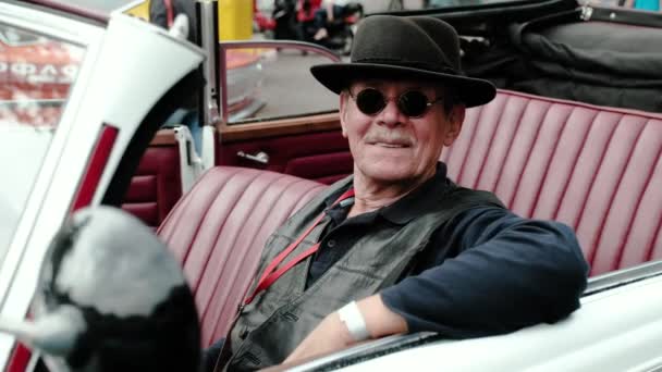 Περιοχή Μόσχα - 16 Σεπτεμβρίου 2018. Ένας ηλικιωμένος άνδρας με ένα καπέλο και ένα δερμάτινο σακάκι πίσω από το τιμόνι ενός αυτοκινήτου ρετρό. — Αρχείο Βίντεο