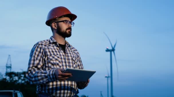 Ingenieur-Baumeister vor dem Hintergrund von Windkraftanlagen am Abend. — Stockvideo