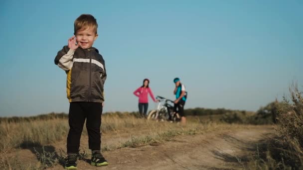 Paseo en bicicleta familiar. Familia fuera de la ciudad. Un niño agitando una pluma en el fondo de los padres con bicicletas . — Vídeos de Stock