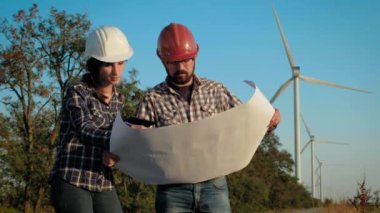 İki mühendis canlı planı büyük bir kağıt parçası üzerinde tartışmak ve notlar. Rüzgar jeneratörleri üzerinde arka plan vardır