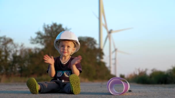 Un niño juega con el casco del constructor. Se lo pone y aplaude alegremente — Vídeos de Stock