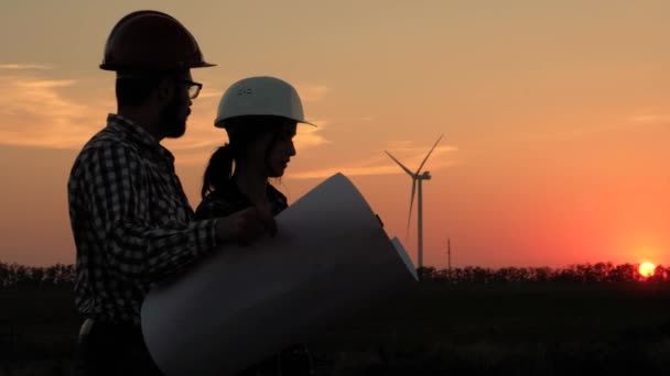 Silhouetten van twee ingenieurs, het uitvoeren van berekeningen op een groot stuk papier tegen de ondergaande zon — Stockvideo