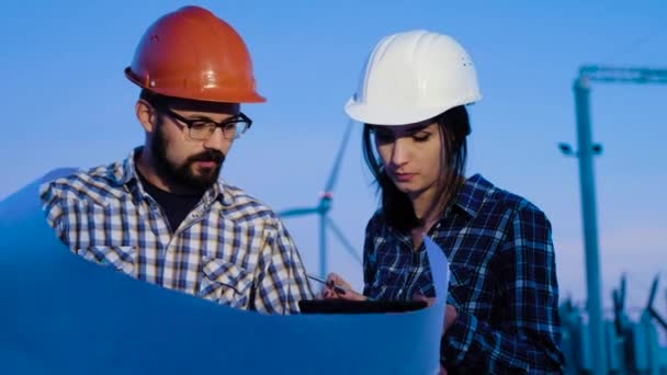 Una mujer y un hombre, dos ingenieros hacen cálculos en una hoja grande de papel, mirando a su alrededor y comprobando la información en la tableta — Vídeo de stock