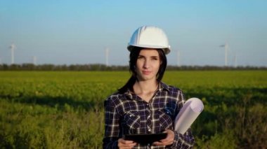 İnşaat kask içinde ve büyük kağıt rulo ile genç bir kadın ve bir alanda standları düz görünüyor. Ağır çekim