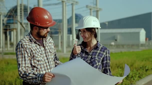 Dois engenheiros discutem plano de aprovação em grande pedaço de papel. A planta está no fundo. Movimento lento — Vídeo de Stock