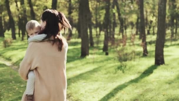 Jonge moeder spinnen met haar zoon in haar armen in herfst park — Stockvideo