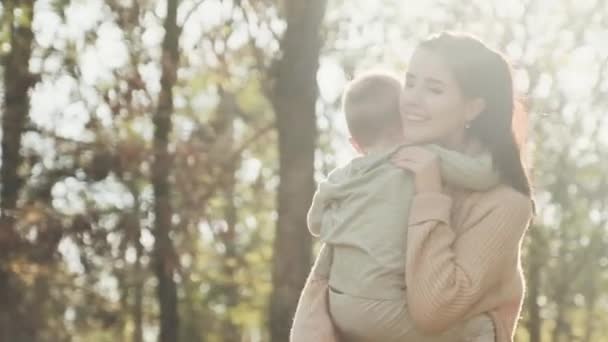 Молода мати крутиться зі своїм сином на руках в осінньому парку — стокове відео