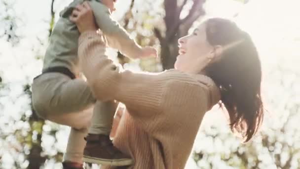 Young mother is spinning with her son in her arms in autumn park — Stock Video