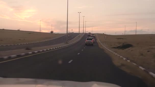 在沙漠日落时, 在行驶道路上行驶的吉普车上可以看到汽车 — 图库视频影像