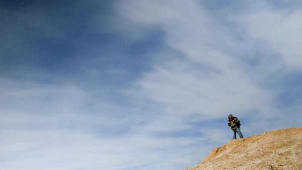 En resenär mot bakgrund av en vacker blå himmel gick till kanten av sandstranden stenbrott, tog ut sin smartphone att orientera sig på terräng och fortsatte att gå vidare. — Stockvideo