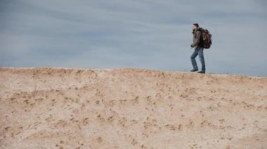 Bir turist için büyük bir sırt çantası ile görme gözlük kum bir Höyük güzel bir mavi gökyüzü arka plan üzerinde yürür..