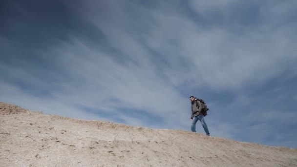 大型バックパックを視力の眼鏡の観光客は、美しい青空を背景に砂のマウンドに沿って歩く. — ストック動画