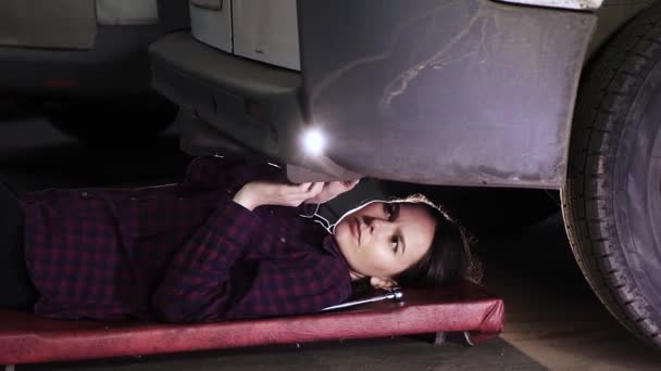 krásná dívka, brunetka, leží pod auto a utahuje šrouby.