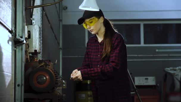 Vacker flicka i en rutig skjorta, svart hjässa och skyddsglasögon, arbetar på en slipmaskin. Kvinna i manlig yrket — Stockvideo