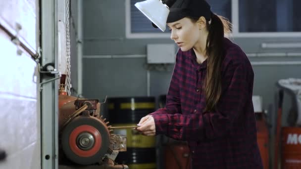 Une fille en chemise à carreaux et un capuchon noir se tient à la machine-outil et effectue des outils d'affûtage. Femme faisant un travail d'hommes — Video