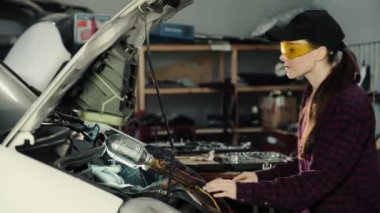 Güzel kız makinist, esmer, ekose gömlek ve koruyucu gözlük bir araba motoru tamir kap. Kadın ve erkek eşitliği kavramı