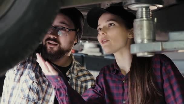 Un joven, un colega, comparte su experiencia con una hermosa chica, un nuevo empleado de una estación de servicio, cómo reparar un coche — Vídeos de Stock