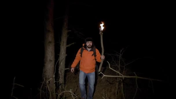 Un touriste perdu dans les bois. Un homme vêtu d'une veste brillante et avec une torche brûlante dans les mains passe la nuit dans une forêt dense à la recherche du salut — Video