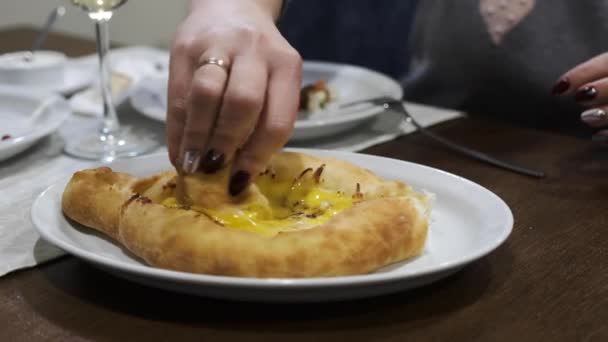 Las manos bien cuidadas de las mujeres envuelven un pedazo de khachapuri en un huevo de gallina crudo. Cocina nacional georgiana — Vídeos de Stock