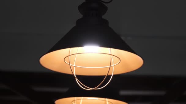 Warme elektrische licht komt van decoratieve lampen geschilderd zwart en oranje op een donkere achtergrond, die boven het plafond worden bevestigd. — Stockvideo