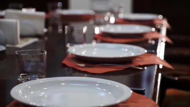 Establecimiento de mesa en un prestigioso restaurante. Placas limpias y blancas, copas de vidrio en servilletas marrones y mesa de madera pulida . — Vídeos de Stock