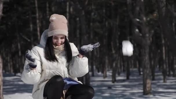 Krásná dívka v borovém parku má zimní zasněžené počasí, hravě spadla do náručí sněhu nad její hlavou, která krásně rozpadne a změní v malé sněhové vločky — Stock video