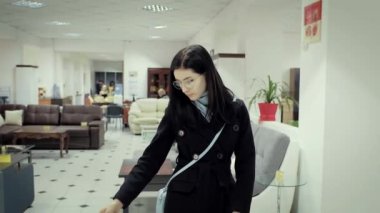 Genç kadın bir mobilya mağazasında siyah paltolu mobilya seçer.