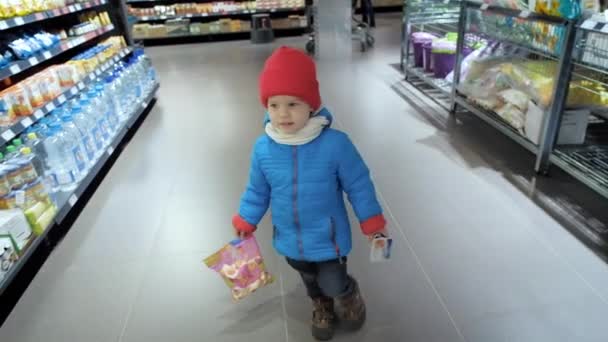 Lille pojken håller godsaker och går genom snabbköps hallen — Stockvideo