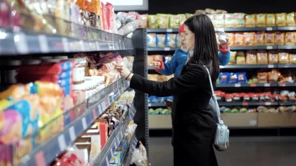 Mamá en un estante de supermercado elige comida para su hijo — Vídeo de stock