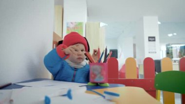 Küçük bir çocuk odasında sıcak giyinmiş kalemler albümde çizer..