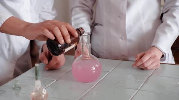 Experimento químico. Personal del laboratorio vertiendo un líquido químico en un frasco con una solución rosa . — Vídeos de Stock