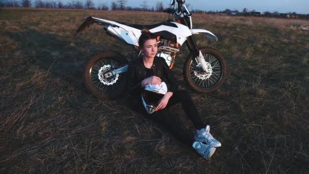 Chica se sienta cerca de una motocicleta y disfruta de la puesta de sol — Vídeos de Stock