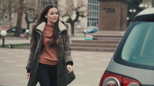 Młoda dziewczyna w jesiennej pogodzie przychodzi do jej samochodu i dostaje za kierownicą — Wideo stockowe