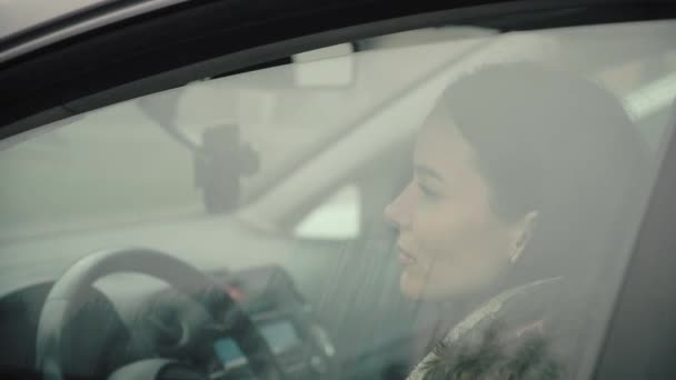 Ένα νεαρό κορίτσι πίσω από το τιμόνι ενός αυτοκινήτου, κατεβάζει την πόρτα του παραθύρου του αυτοκινήτου.. — Αρχείο Βίντεο