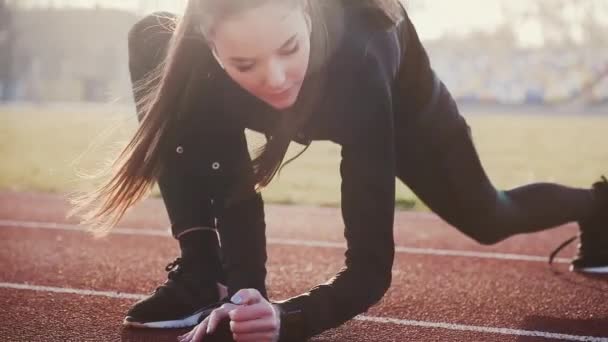 Meisje op het stadion in draadloze koptelefoon voert fitnessoefeningen voor stretching spieren. — Stockvideo