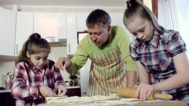 Father shows his two daughters how to roll out the dough. One of the daughters has Down syndrome. — Stock Video