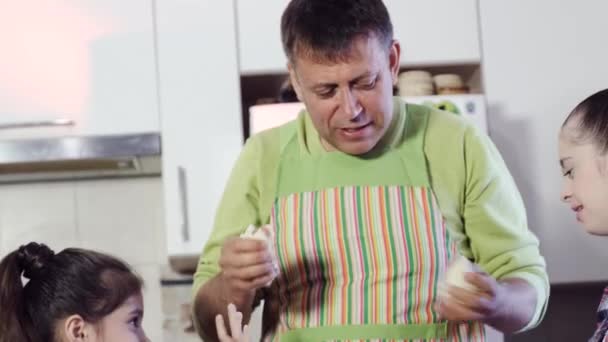 Father of the family gives his daughters, one of them with Down syndrome, a piece of dough — Stock Video