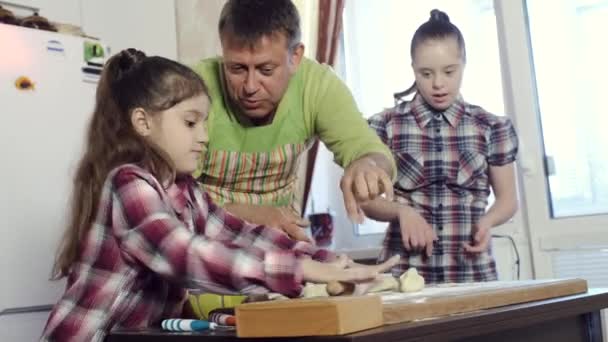 The father of the family teaches his daughters, with Down syndrome, kitchen secrets. — Stock Video