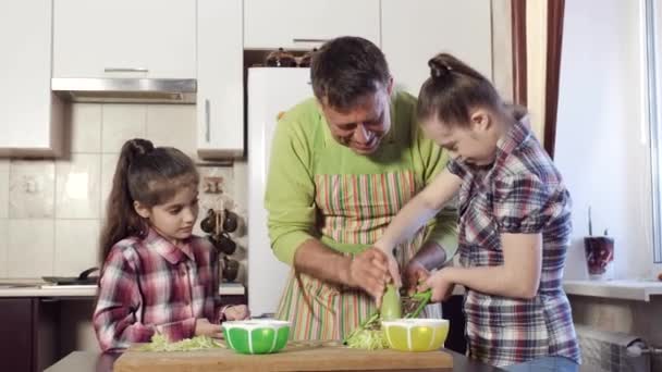 Fadern undervisar sin dotter, som med Down syndrom, hur man korrekt gnugga zucchinin på ett rivjärn. — Stockvideo