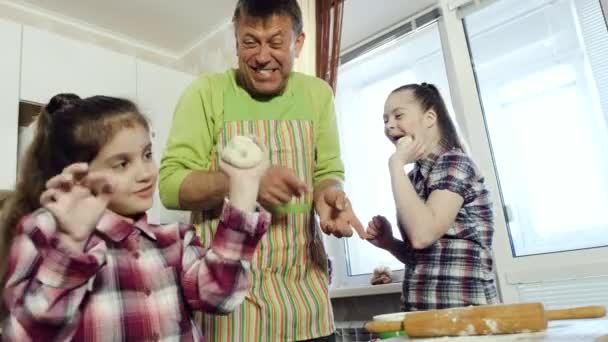 Papi se divierte con sus hijas mientras cocina masa en su cocina casera . — Vídeos de Stock