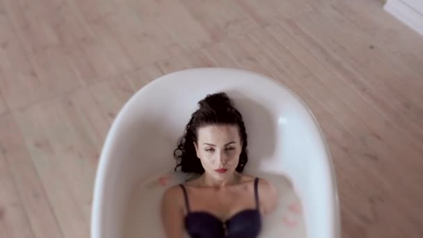 Чудова жінка в бюстгальтері лежить у ванні з молоком і пелюстками квітів — стокове відео