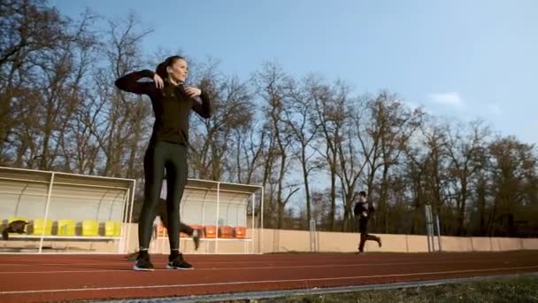 Ein Mädchen macht an einem sonnigen Herbsttag Fitnessübungen auf einem Laufband, auf dem die Menschen laufen. — Stockvideo