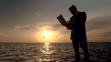 Muhteşem bir gün batımı arka planda denizin ortasında bir laptop ile işadamı.