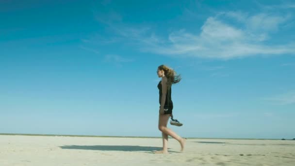 Malá holka v šortkách pěšky po opuštěné pláži kolem slámově hub. — Stock video