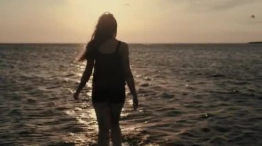 Genç bir kadın nazikçe bir kiteboard arka plan karşı günün gün batımı su girer.